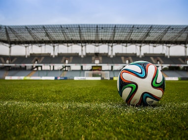 A soccer ball on a field with a stadium in the background.